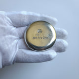 hand poured polished zinc round held in a white glove against a light gray background